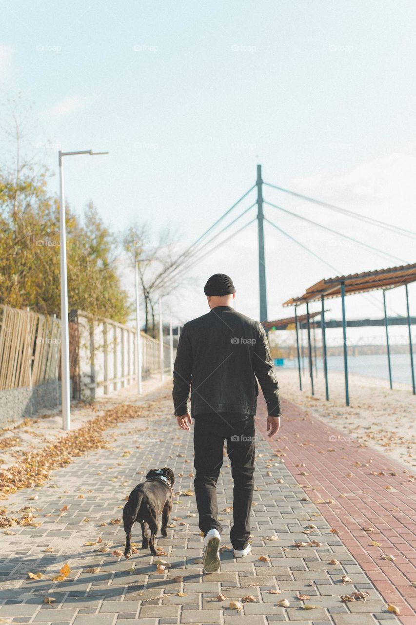 a guy of about thirty-three, walks on the banks of the river with his dog friend. the guys run, walk together, the guy throws a stick to the dog, a warm sunny day. walk with the dog