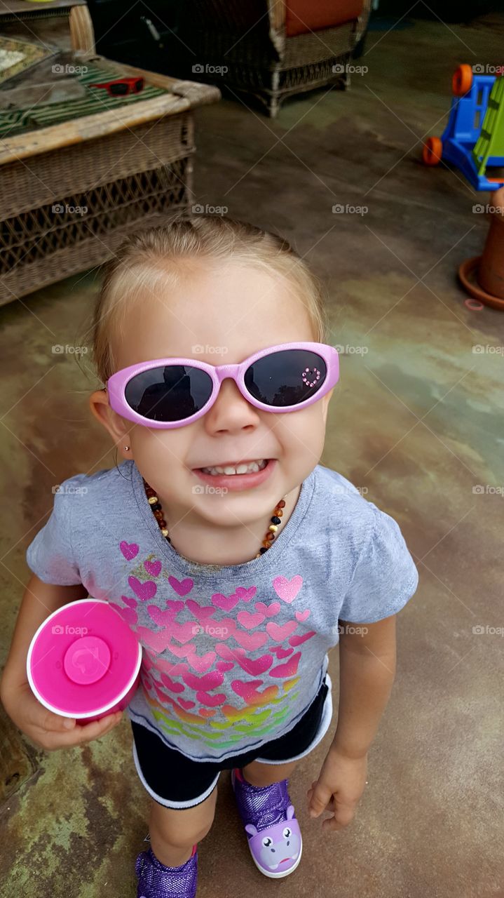 my cute little daughter wearing sunglasses on the back porch patio area in Kingston Tennessee 2017 United States of America smiling big cheesing
