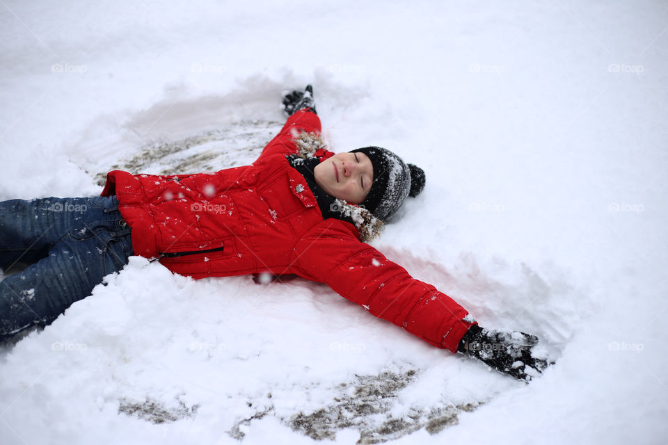 Boy in red jacket makes a snow angel in winter outdoors