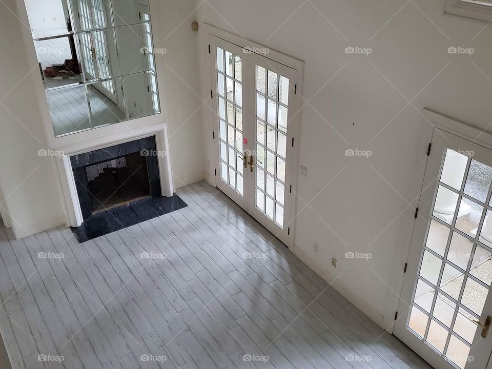 Looking down at a large open white living room with a black marble fireplace and French doors