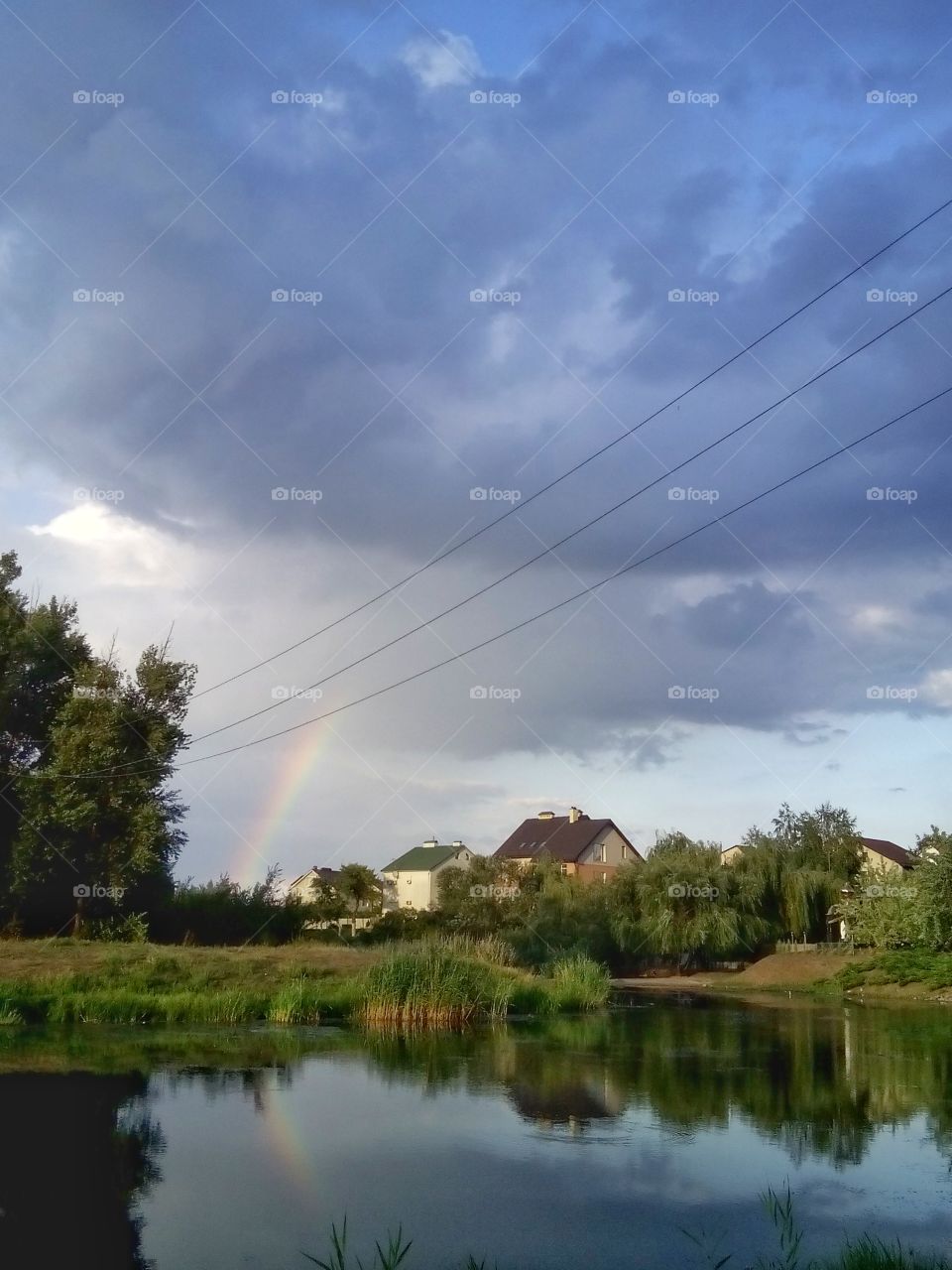 Beautiful landscape.  Houses by the river, the sky with clouds and a rainbow reflected in the river