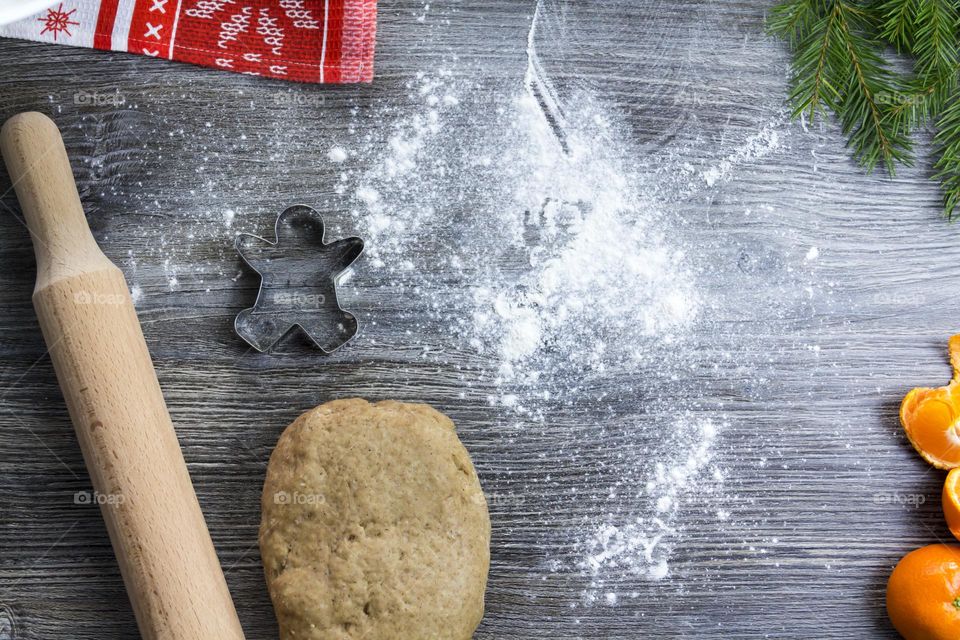 Cooking Christmas gingerbread cookies on a wooden table with tangerines and green Christmas trees.