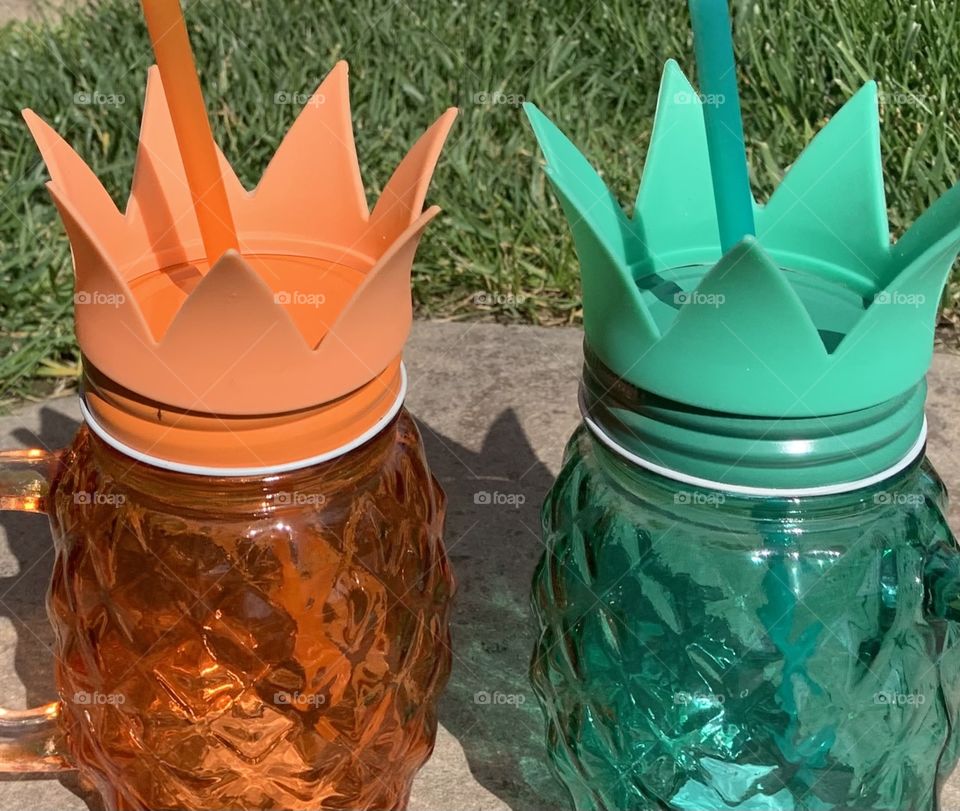 Two pineapple glass mason jar cups with straws outside on the lawn 