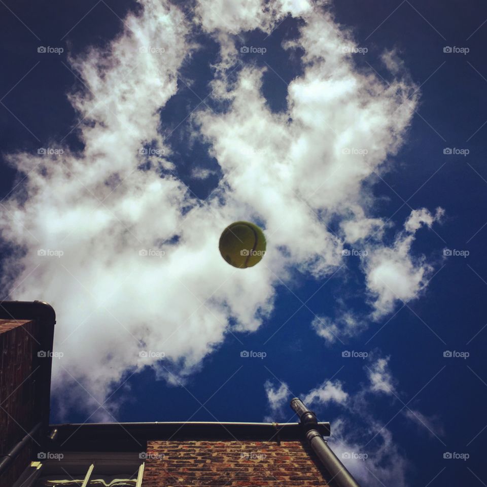 Airborne tennis ball under blue cloudy skies