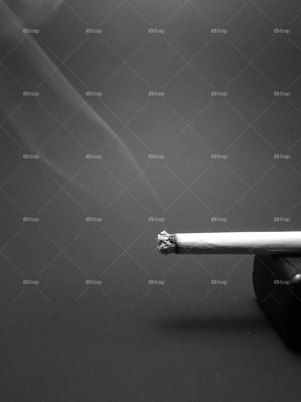 a lit cigarette with billowing smoke photographed in black and white.