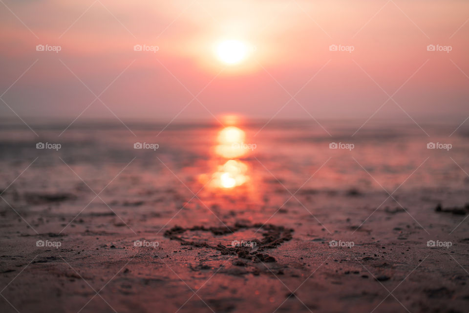 Another photo of the heart drawn in the sand but from a different angle. In front of the heart is a beautiful blurred out sunset and the bokeh is so stunning. The orangey tone perfectly lights up the surrounding sand and produces a nice reflection.