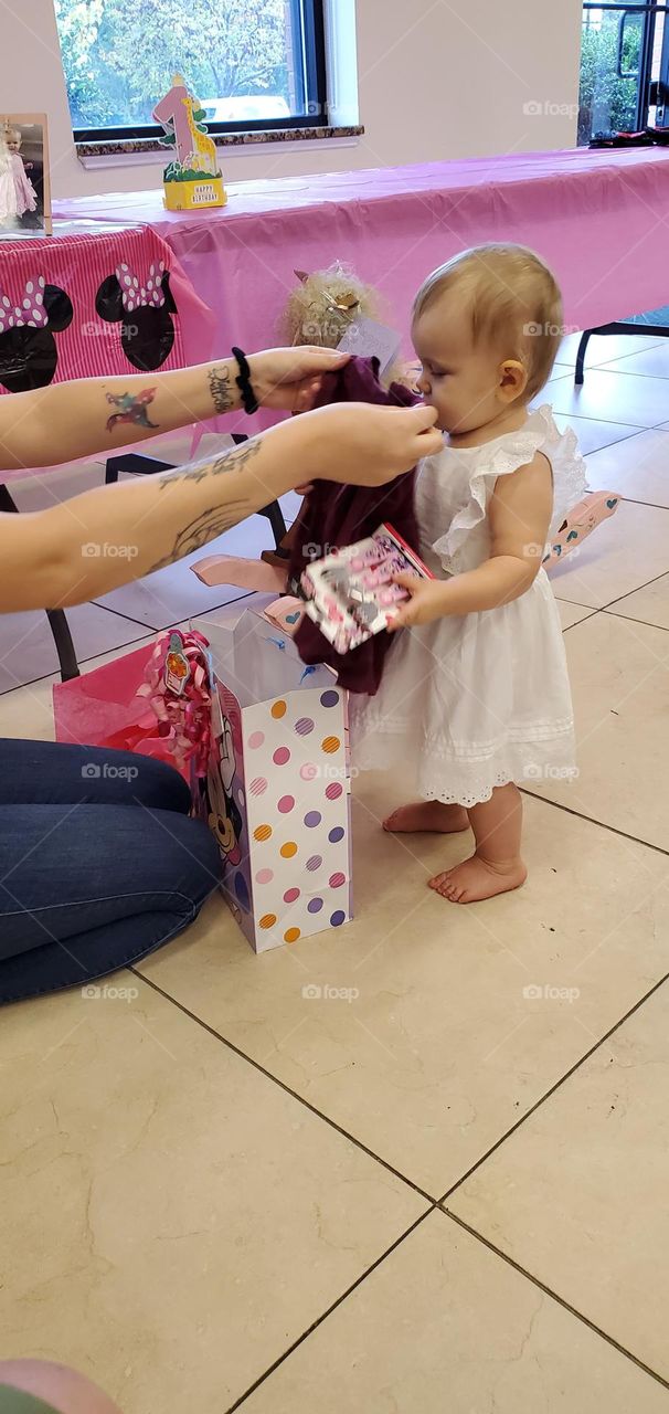 a mom with tattoos on both arms holds up clothing to the toddler which she got as a gift