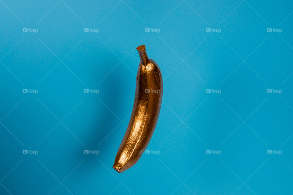 Floating gold banana on blue background. Minimal food concept