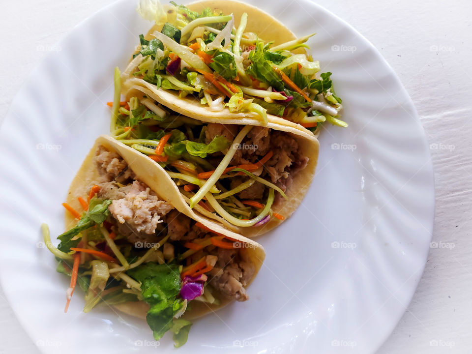 Chicken and cabbage slaw tacos on corn tortillas on a white plate on a white surface