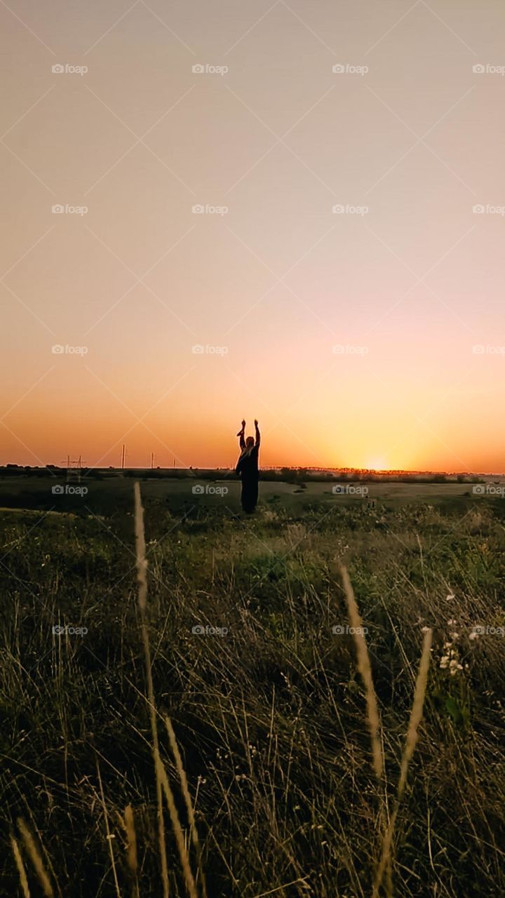 Woman's dark silhouette on the horizon line in the field. Meditation on sunset, deep connection with nature
