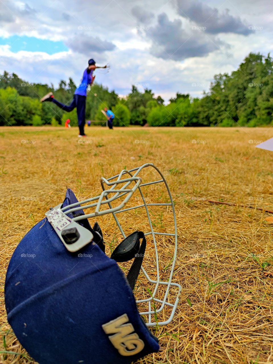 cricket training. On the field lies a protective helmet for playing cricket. In the background of the photograph the player throws the ball