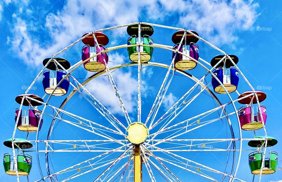 Brightly coloured pods on a Ferris Wheel against a blue sky.
