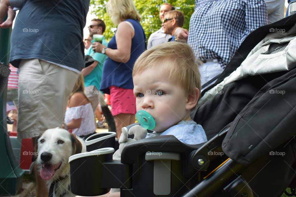 Cute baby boy enjoying Fourth of July parade with crowd of people celebrating Independence Day 