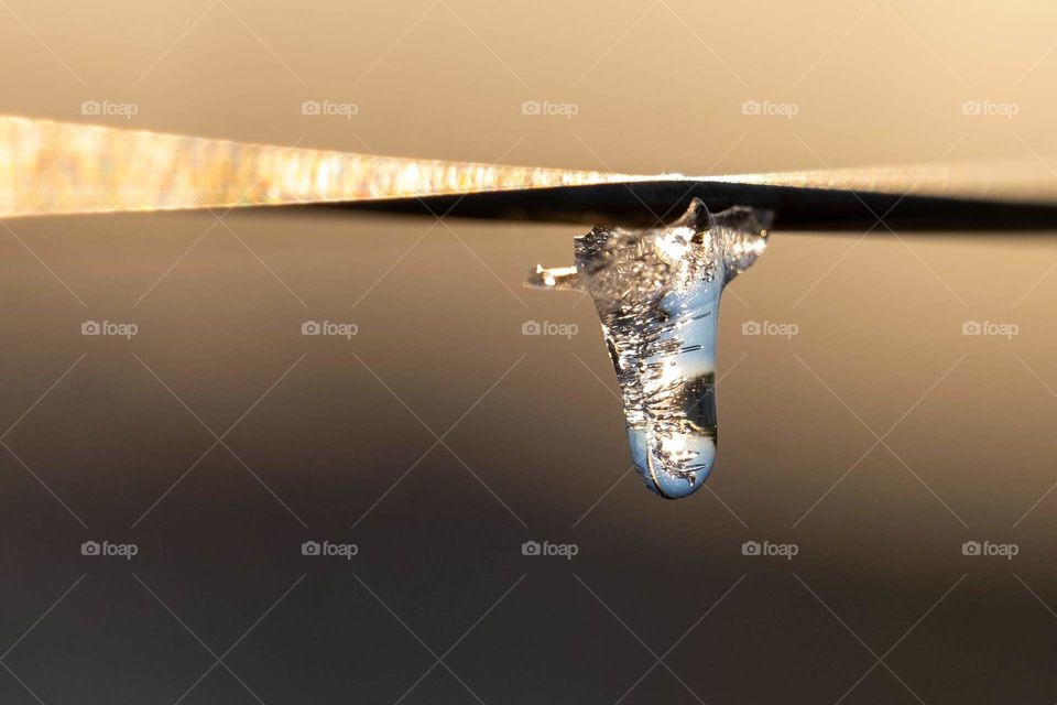 A frozen water drop hanging from an electric fence, with visions of the sky seen in the refractions. 