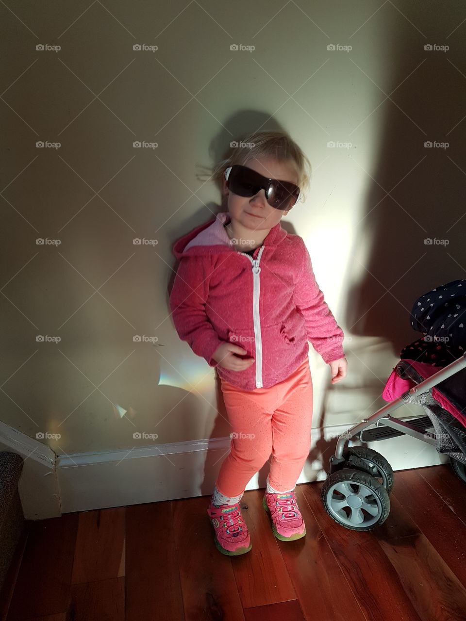 Little girl with sunglasses on wiggling against a wall
