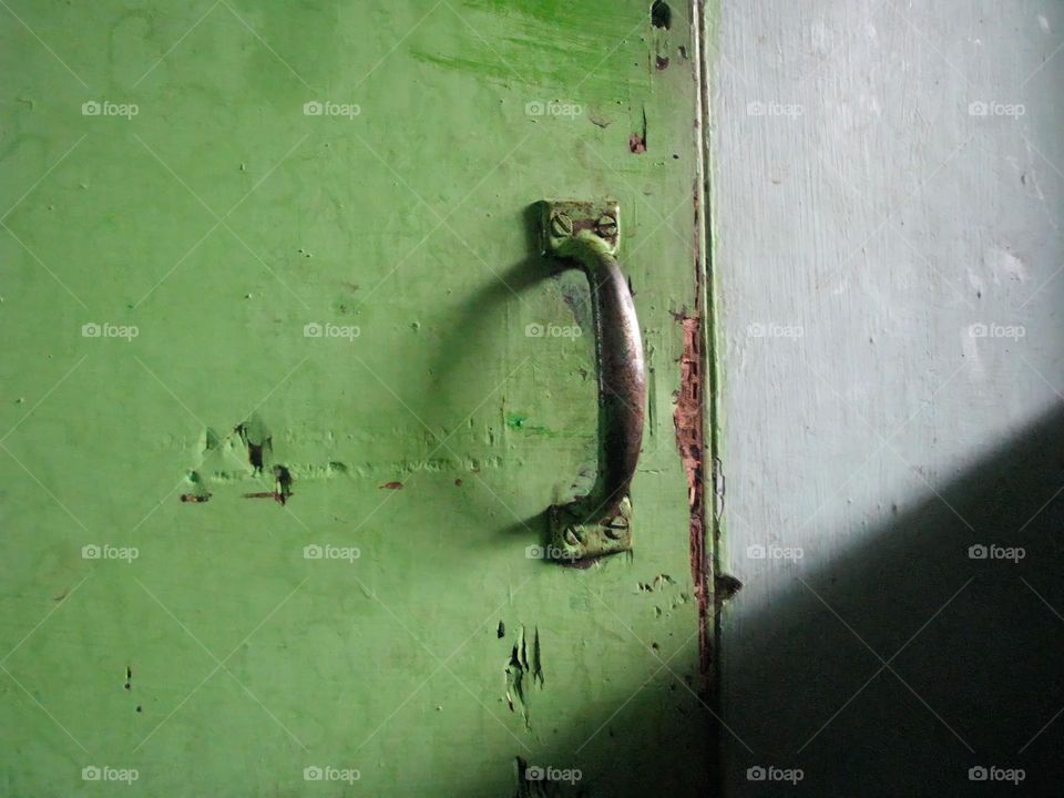 Close-up of a metal door handle attached to a worn and peeling green door in low angle view