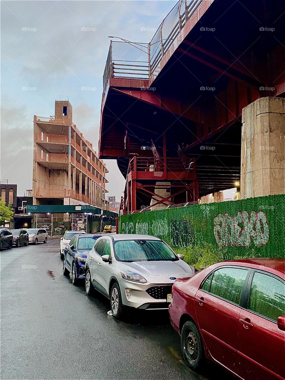 This is the red metal staircase up to the „Pulaski Bridge“ at „Newtown Creek“ seen from underneath on the „Greenpoint“, Bklyn side. On the left there is scaffolding for construction that has been underway for a long time. 2023. Hypnotic Productions