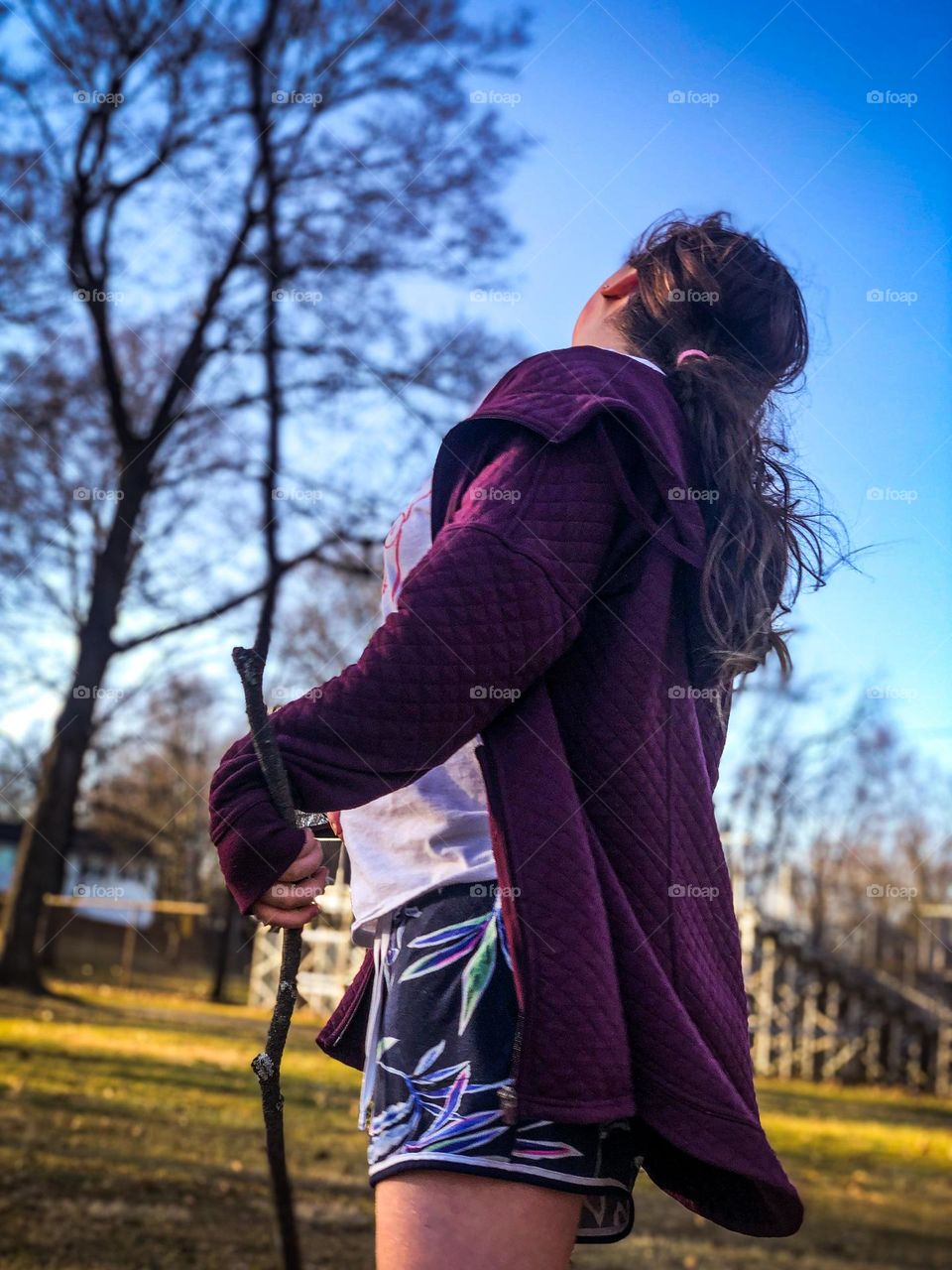 A young lady with her walking stick at the park looking into the tree tops 