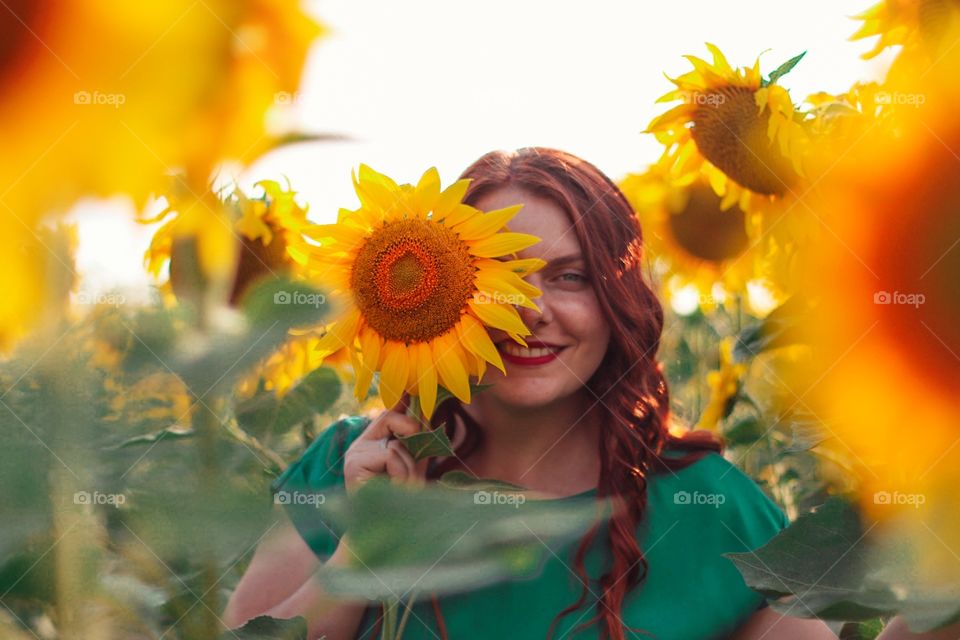 Smiling red-haired girl with a sunflower in her hand in a yellow field in summer