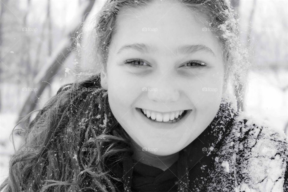 Black and white close up of a beautiful young girl smiling and laughing with freshly fallen snow in her hair. 