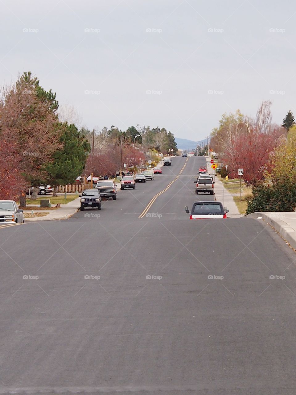 A suburban street full of parked cars bordered by sidewalks, landscaped yards, and road signs in Central Oregon. 