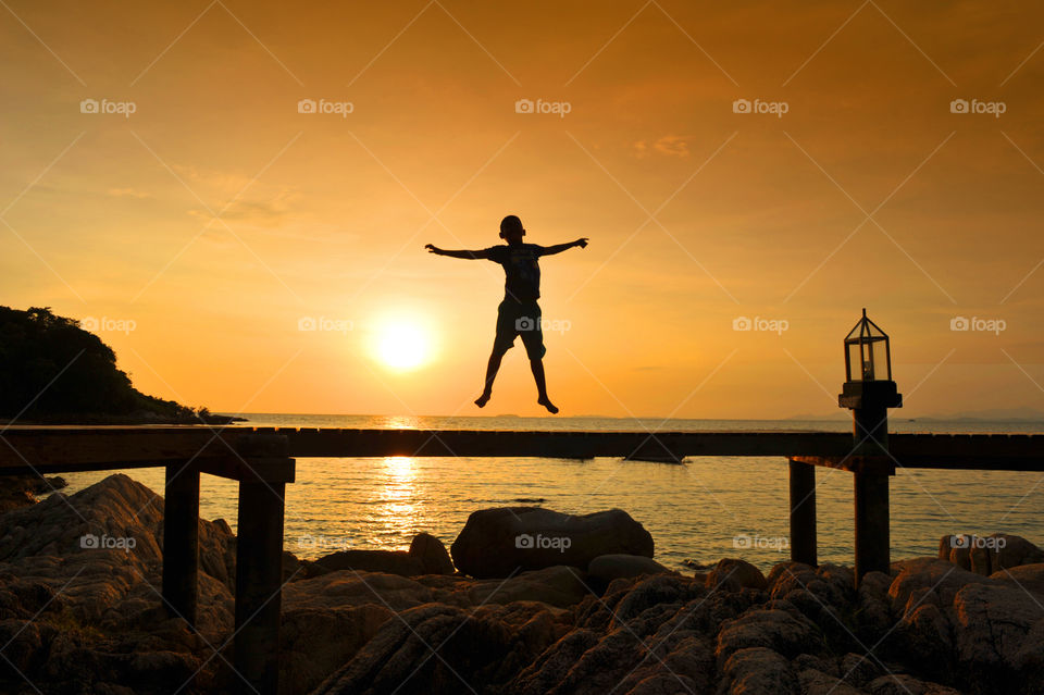 Boy jumping in silhouette by the sunset sea