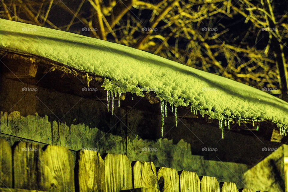 ice hanging off the edge of a snow covered rooftop on a cold winters night