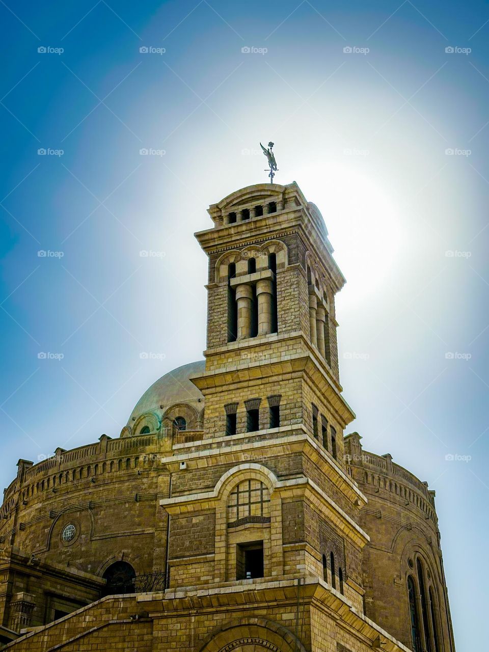 The bell tower of the Hanging Church in Cairo, set against the backdrop of a sunlit sky and a halo effect.