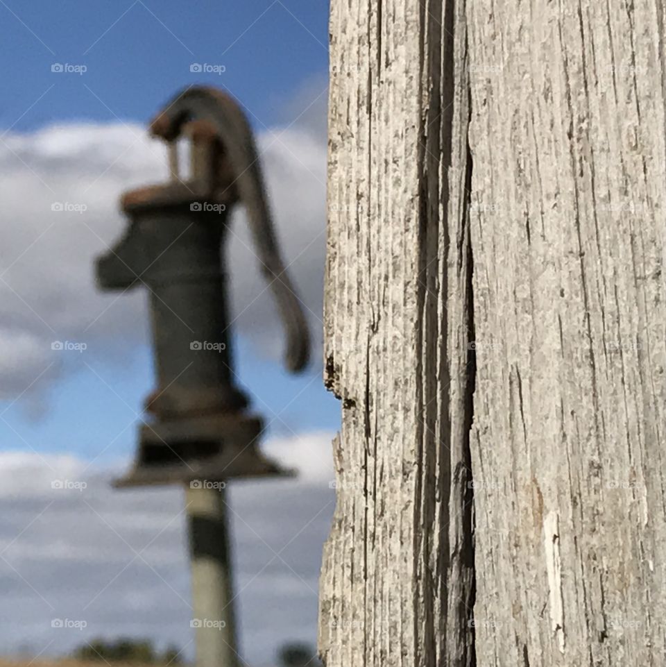 Focusing on the old wood siding of a shed with an old style water pump in the distance.