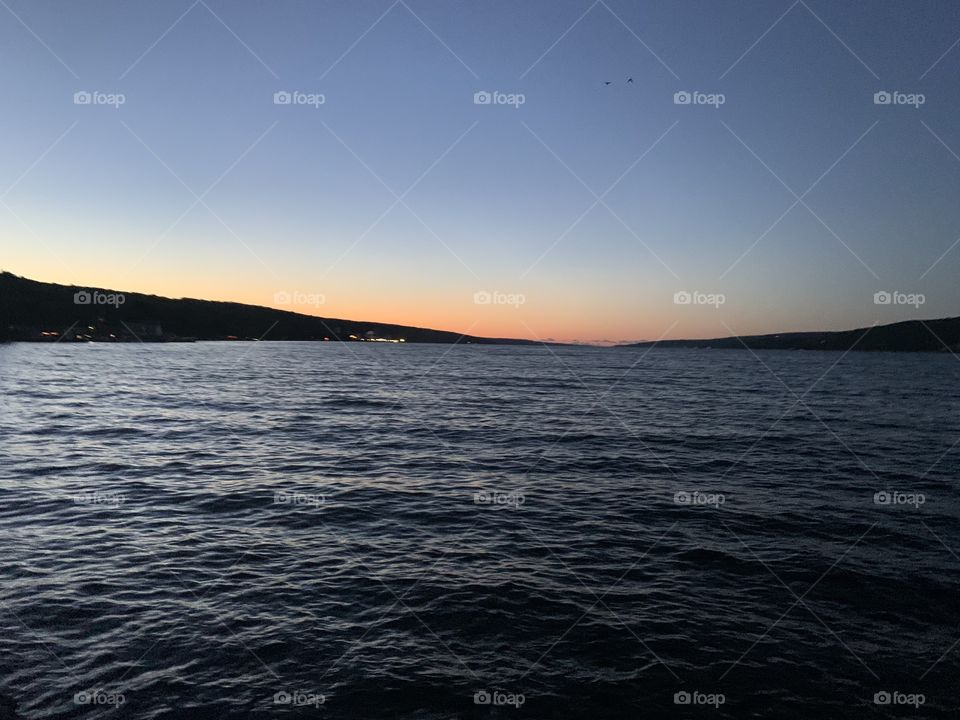 An orange sunset over calming water with beautiful a beautiful sky, hill, and lake.  