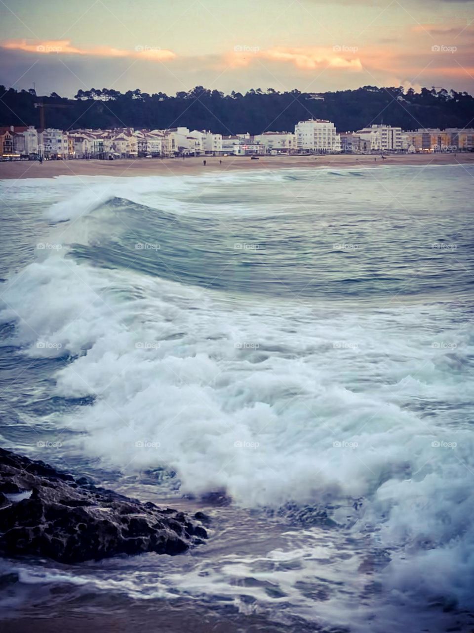 Waves roll in on Praia da Nazaré, with seafront buildings in the distance