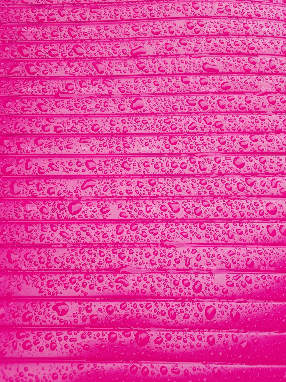 Close up of water droplets on a wet shiny plastic surface pink with horizontale lines parallele
