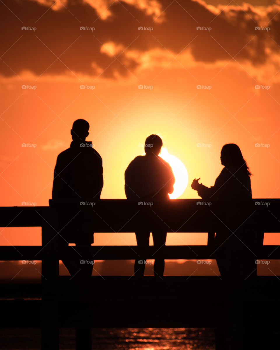 Friends enjoying a beautiful golden sunset on the water. Silhouetted figures standing on a pier. 