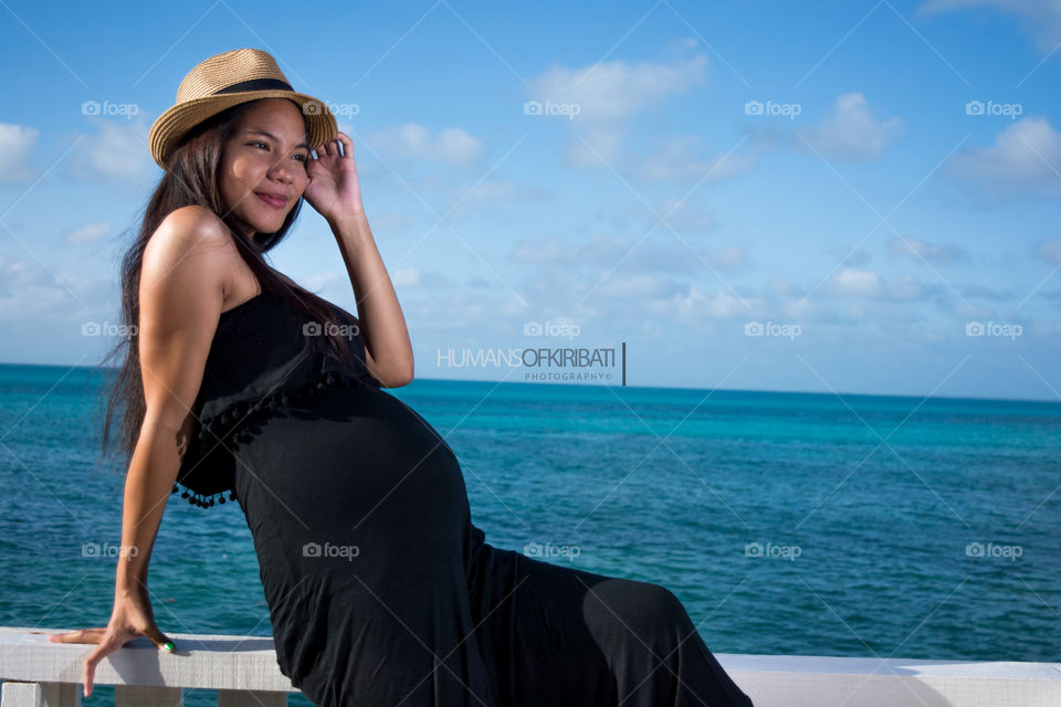 Young pregnant woman sitting on railing wearing hat