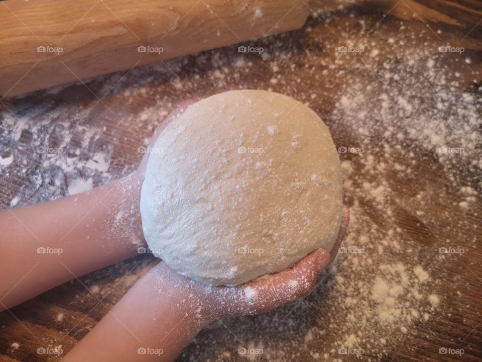 The child holds the pizza dough