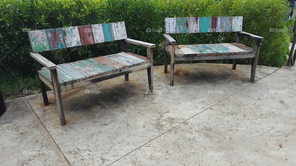 two benches made from recycled boards on a concrete deck in front of green hedges.