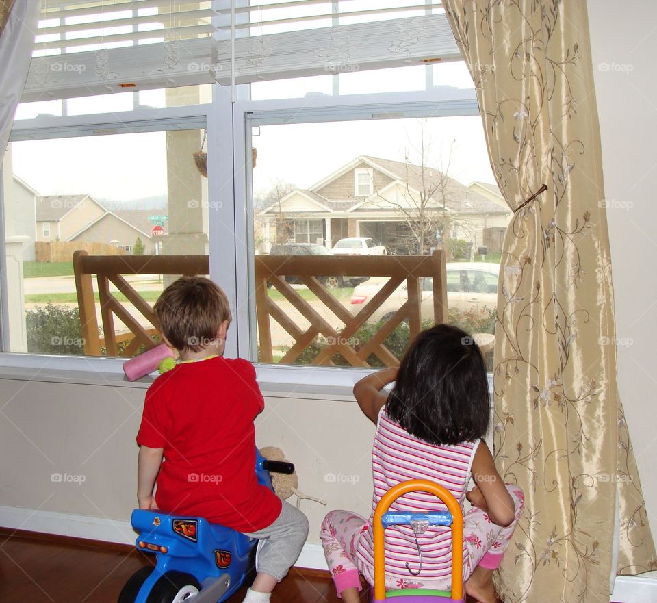 Two children playing in the living room by the window