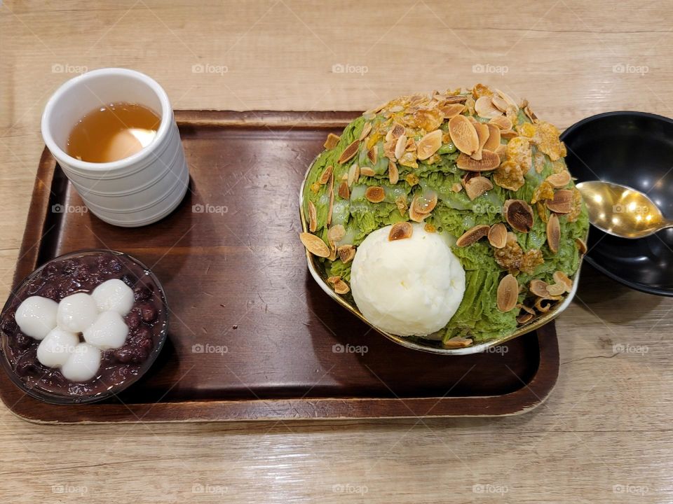 Matcha-flavored shaved snow with ice cream, sprinkled with sliced ​​almonds, dangos and sweet red beans, with a cup of tea.