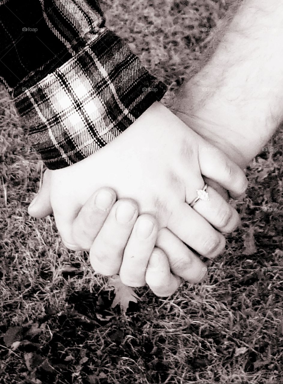 A couple holds hands in a show of love and affection, displaying a marquis cut diamond engagement ring.