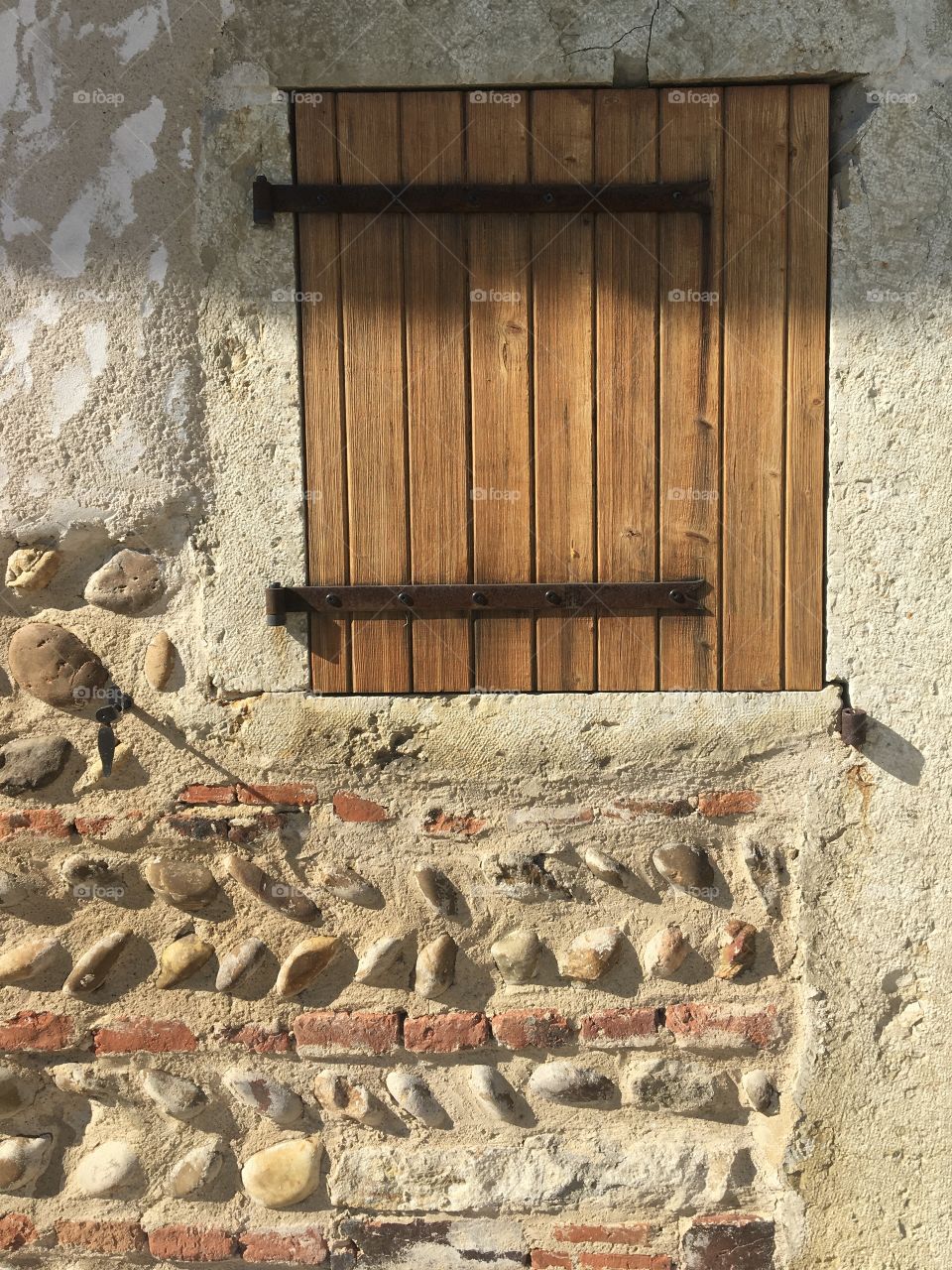 Closed wooden shutters and traditional wall made with river pebbles