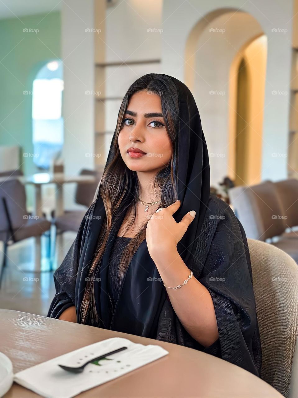 Close-up of young woman eating in a restaurant or cafe. She wore black clothes and jewelry on her right hand. In front of him was an empty plate with a green design and silver cutlery