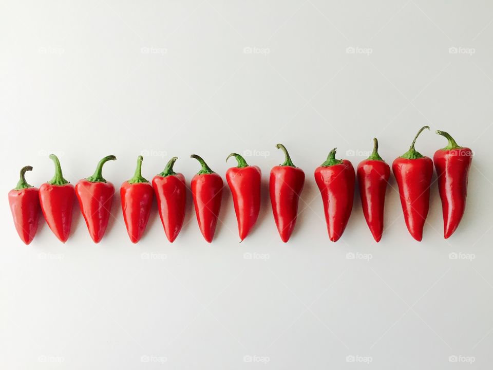 Minimalistic Snaps - Flat lay of red chili peppers, arranged horizontally by size on a white surface 