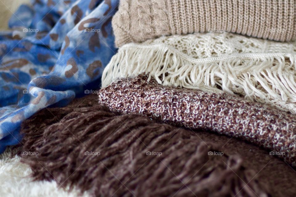 Cable knit, crocheted and fringed sweaters in taupe and brown and a blue tye-dyed leopard-print scarf on a sheepskin throw 