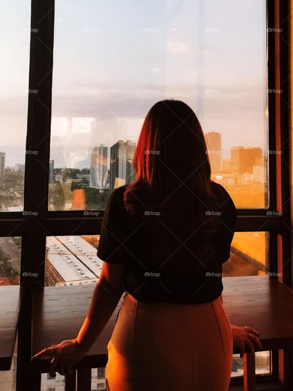 Portrait of young woman looking at city view at sunset from large window