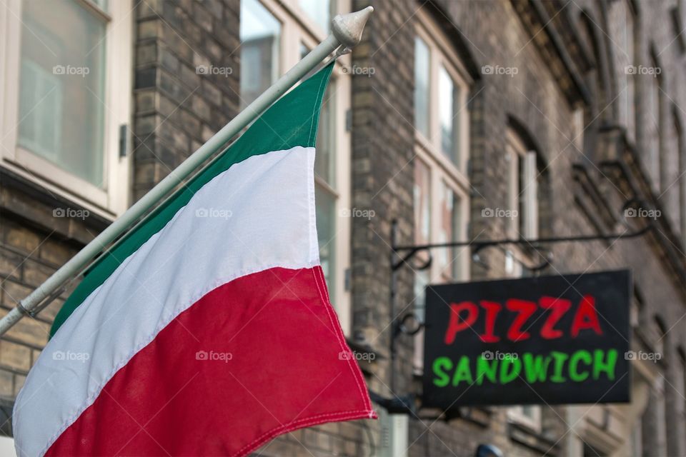 Italian flsg hanging frim a building with the sign pizza sandwich in the background