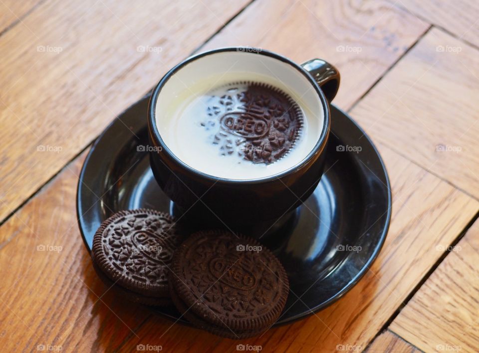 Oreo cookies with milk in black cup.