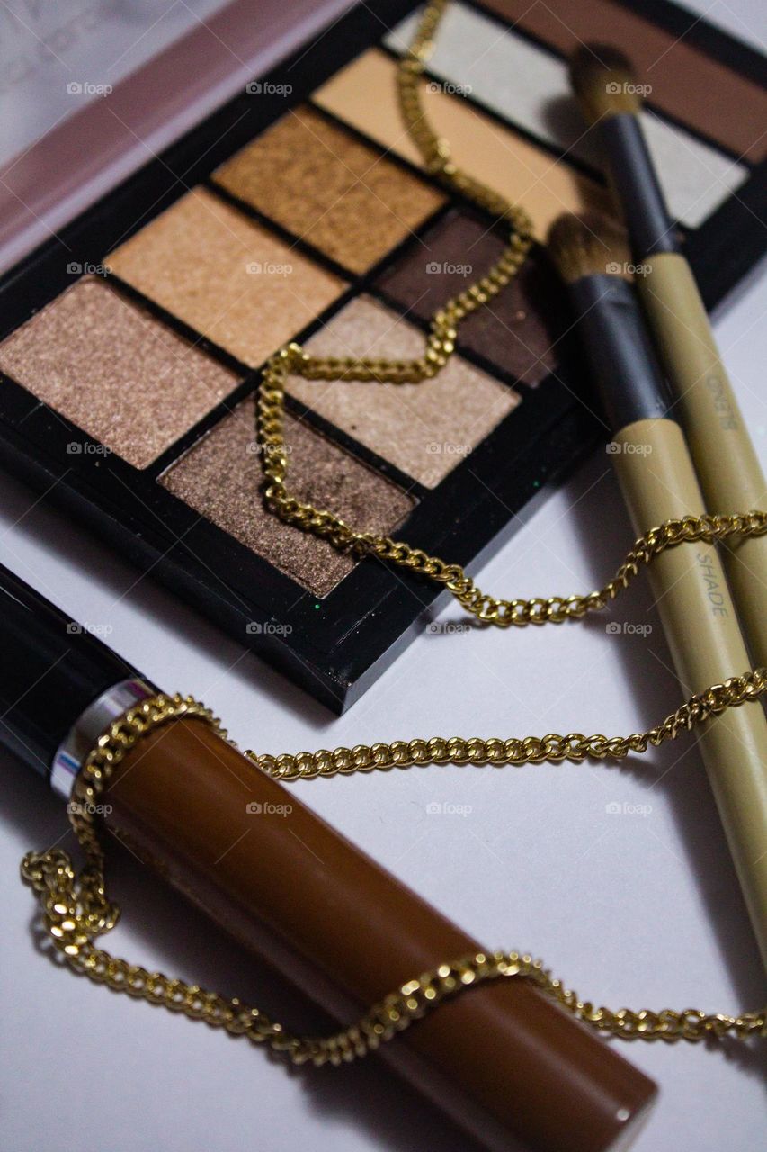 Beautiful neutrals. A makeup palette of natural colors. Eye shadow, mascara, and application brushes, with a gold chain necklace.