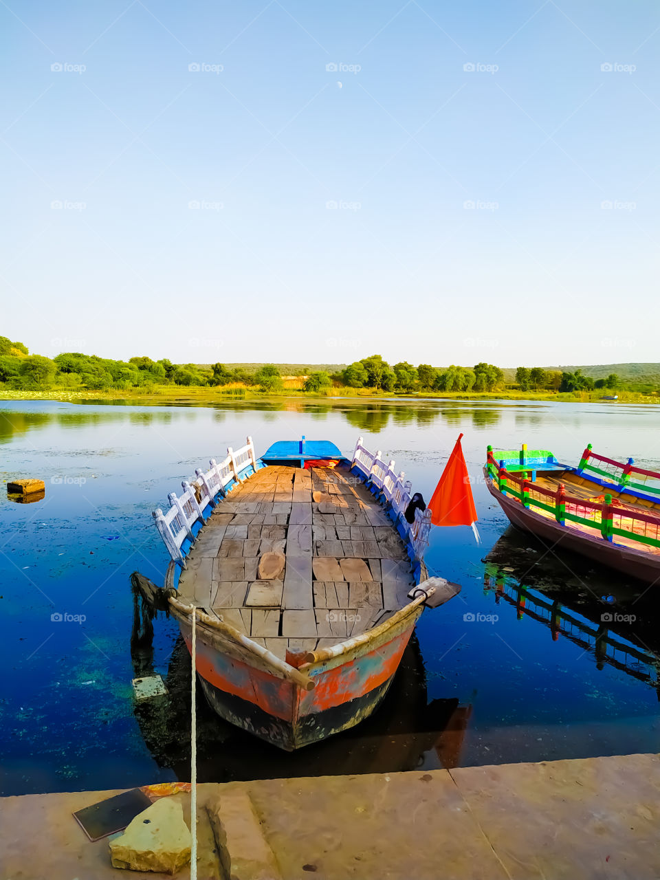 Two wooden boats parked along the river with green trees and green hills in the site behind the river