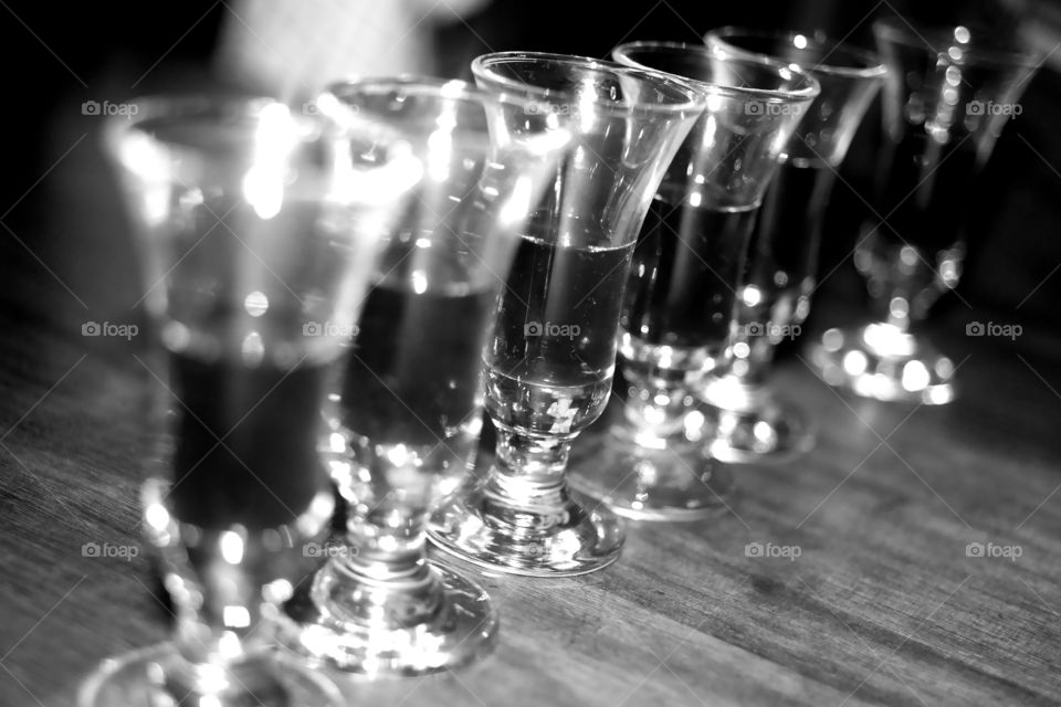 Six little shot glasses, standing in a row.  The party is underway. The glasses are filled with a dark drink. maybe Kahlúa? Maybe Port? Maybe Sambuca? Maybe even Jägermeister? Drink up!