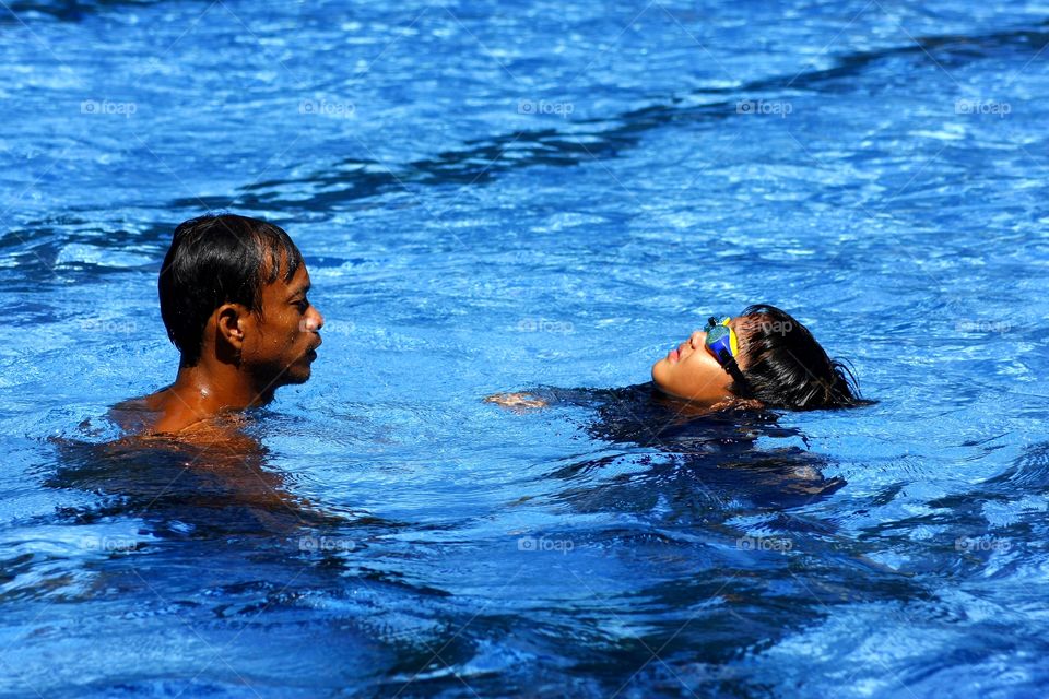 coach teaching a boy how to float in a swimming pool